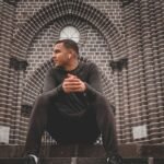 man in black long sleeve shirt and black pants sitting on brown brick wall